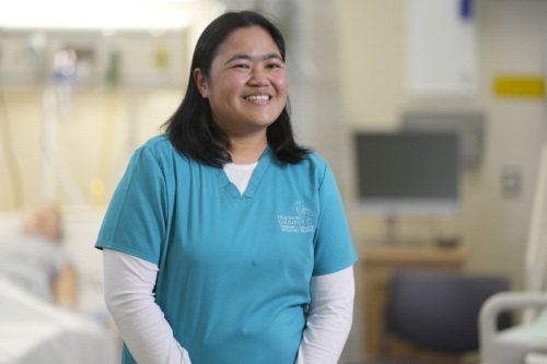 Eunice, a New Jersey Pay It Forward Fund participant, smiles at the camera. She is in a hospital room wearing blue scrubs.